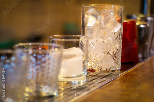 ice in a glass standing on the bar and a few empty glasses in defocus. copy space