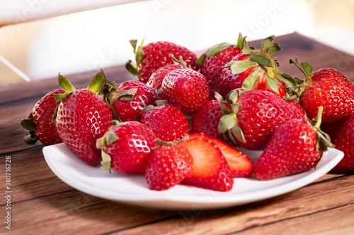 Strawberries on a white square plate on a wooden table in a rustic setting