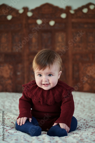 Adorable baby on bed with wooden headbed.