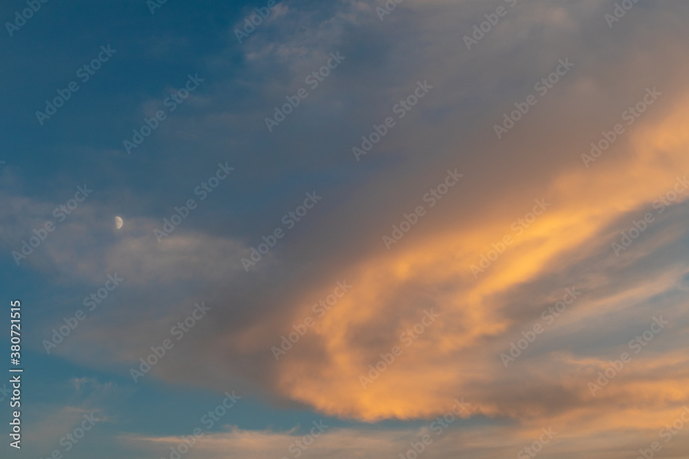 Sunset colorful epic colorful golden clouds on blue vivid sky with early moon. Magic dusk light cloudscape