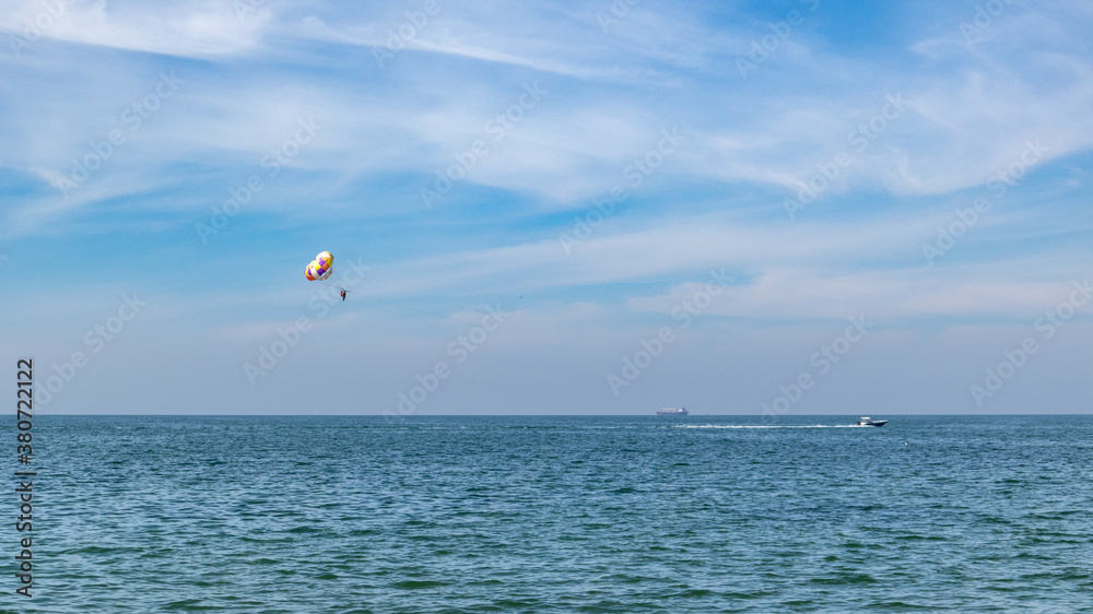 Parasailing on a colorful parachute with boat on sea in blue cloudy summer day. Water vacation Parasailing on a colorful parachute with boat on sea in blue cloudy summer day. Water vacation