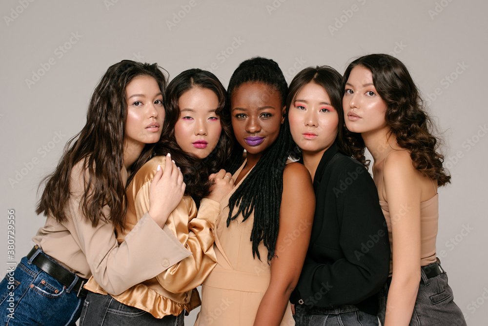 Multicultural shinning girls are sitting together on the grey background Multicultural shinning girls are sitting together on the grey background