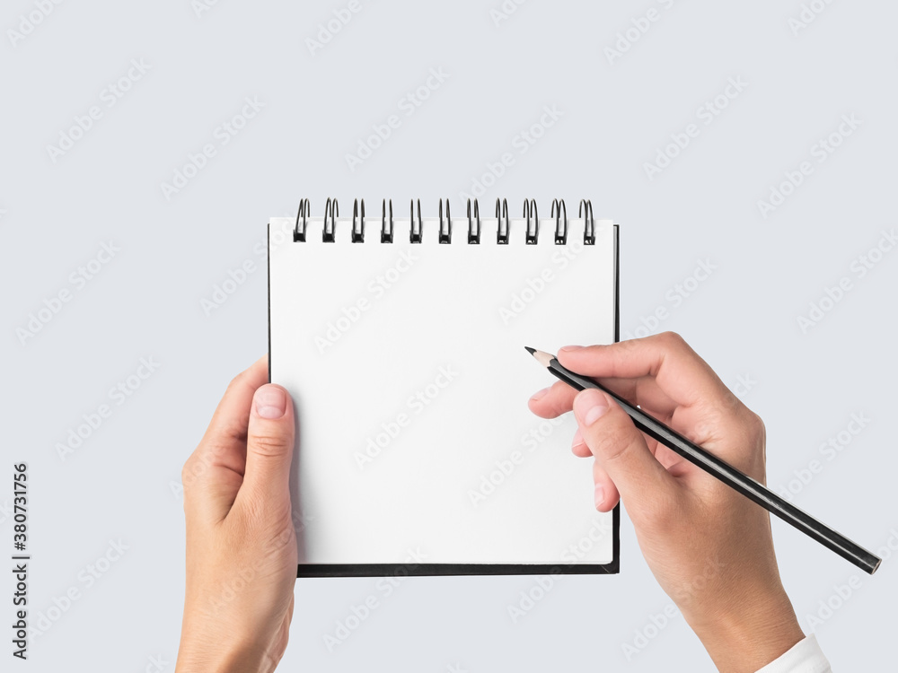 hands holding a square spiral notebook with blank white pages on gray isolated background. woman is going to write notes in notebook with black pencil. mockup, space for text. education concept hands holding a square spiral notebook with blank white pages on gray isolated background. woman is going to write notes in notebook with black pencil. mockup, space for text. education concept