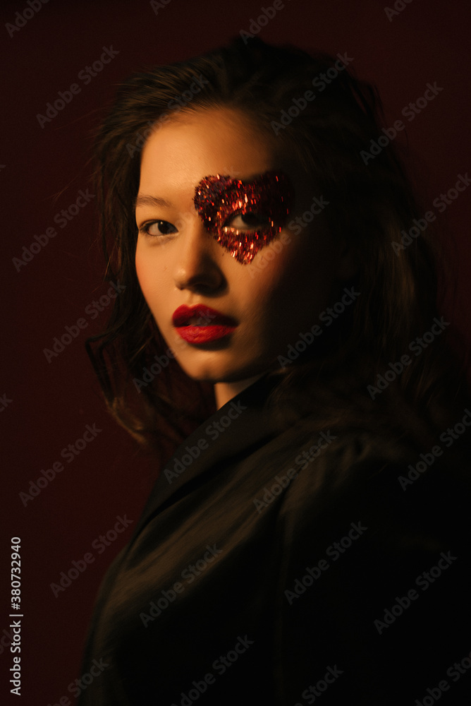 Closeup portrait of an asian girl in the dark with heart-shaped red glitters around her eye and red lipstick in black silk dress Closeup portrait of an asian girl in the dark with heart-shaped red glitters around her eye and red lipstick in black silk dress