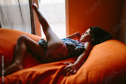 Kid lying on an orange cushion by a window photo