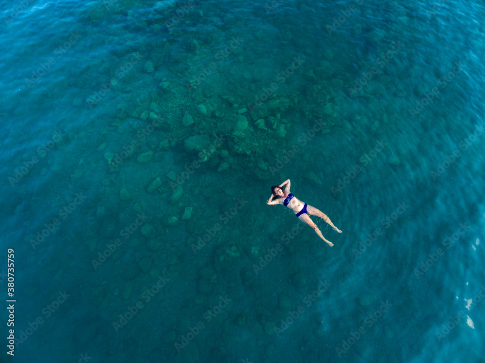 aerial image of a woman floating in dark turquoise water aerial image of a woman floating in dark turquoise water