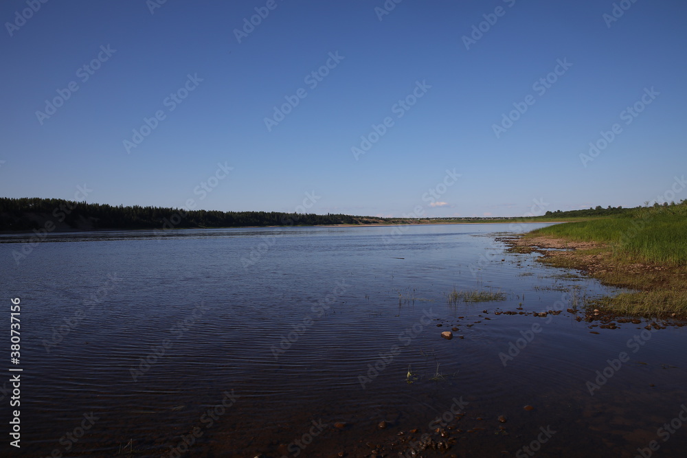 Beautiful water landscape with ripples on the surface of the water with a green shore and pine trees on the horizon.Soothing view of the spacious river on a summer day.Russia Beautiful water landscape with ripples on the surface of the water with a green shore and pine trees on the horizon.Soothing view of the spacious river on a summer day.Russia