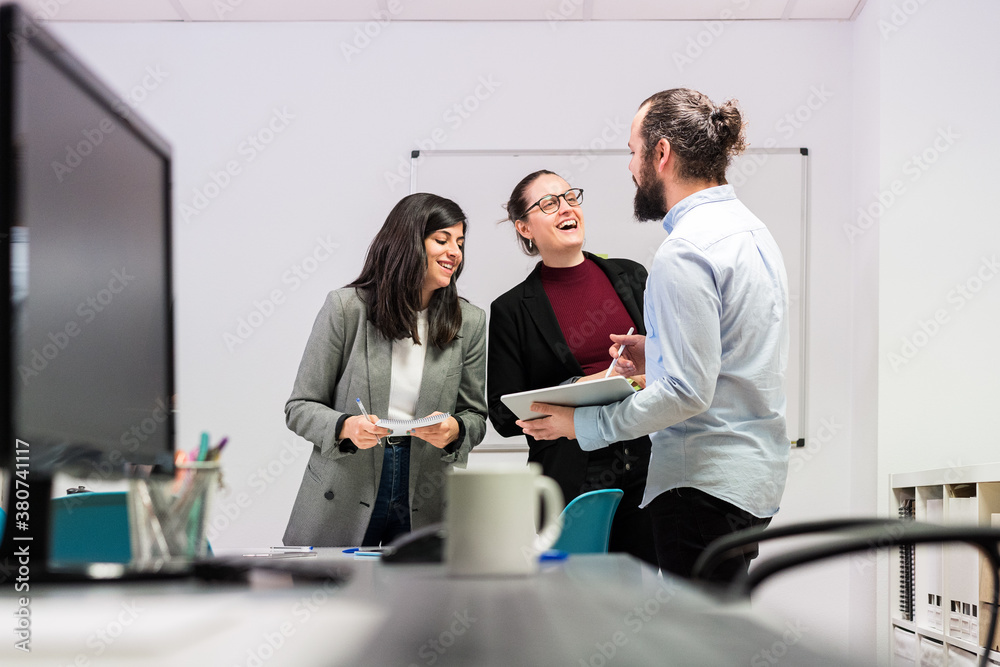 Group of positive young colleagues in formal clothes gathering in contemporary coworking office with tablet having break during work Group of positive young colleagues in formal clothes gathering in contemporary coworking office with tablet having break during work