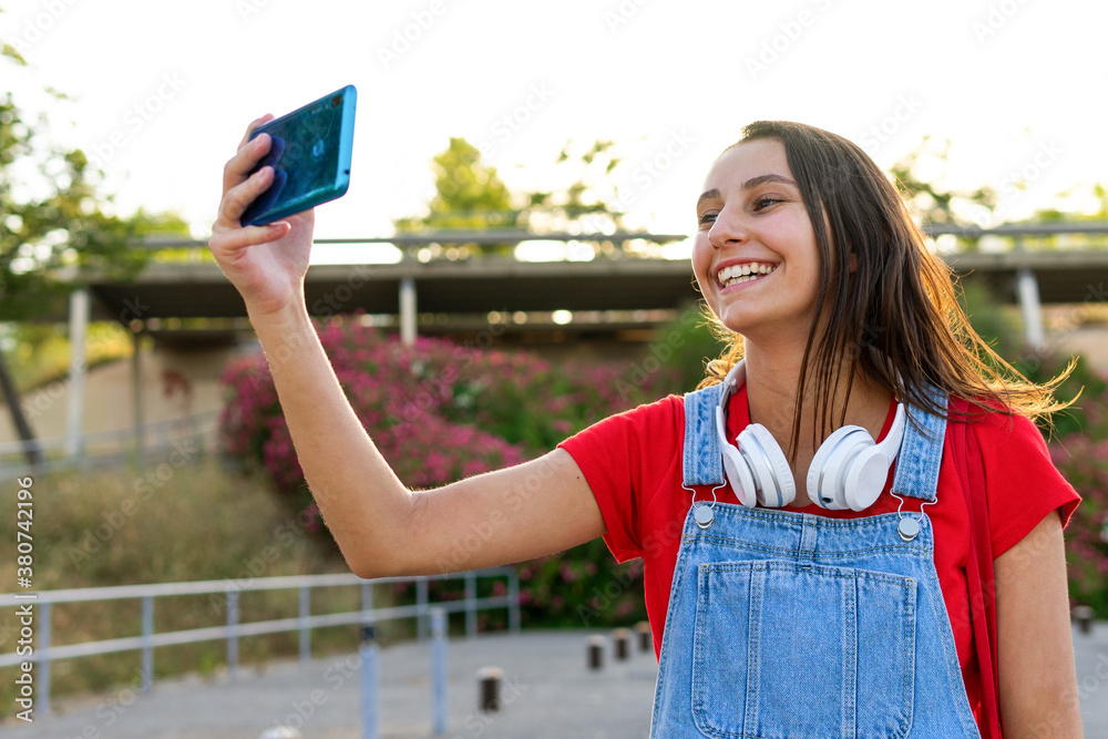 Smiling female millennial standing in city and taking photo on cellphone selfie camera