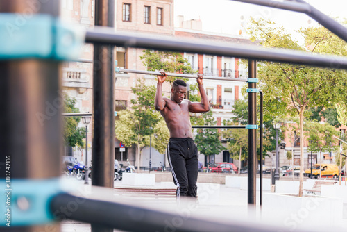 Focused African American male athlete doing pull ups on crossbar during intense training on sports ground in city