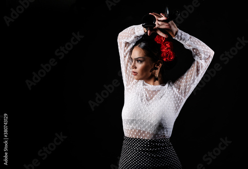 Young Hispanic woman in white blouse performing traditional Flamenco dance with castanets in raised arms photo