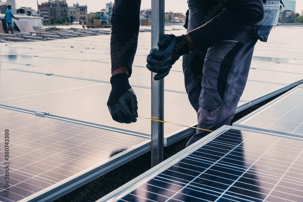Workman in protective uniform installing modern solar panels on roof of industrial building Workman in protective uniform installing modern solar panels on roof of industrial building