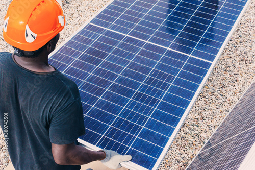 Back view of unrecognizable African American worker walking with solar panel on sunny day in industrial area photo