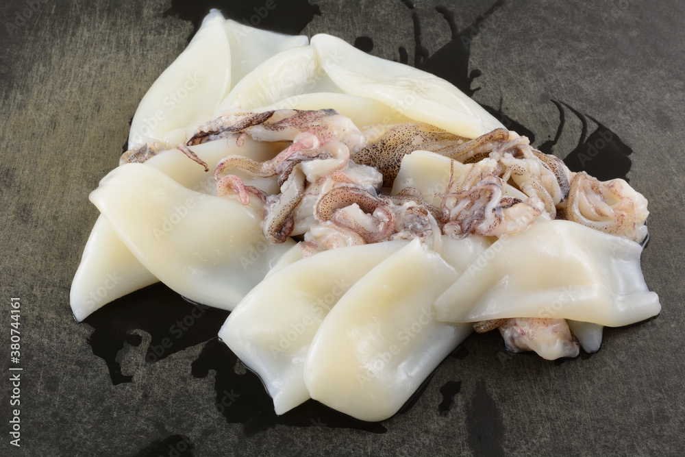 Closeup of raw squid tubes and tentacles on weathered black cutting board