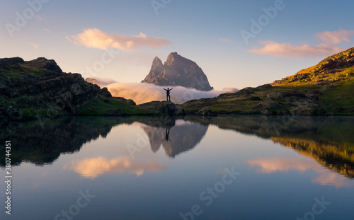 Silhouette of carefree tourist standing with outstretched arms on rock near lake and enjoying freedom in mountains during sunset
