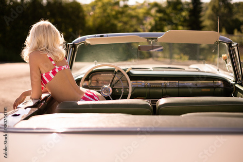 Back view of anonymous woman in striped swimwear peeking out from retro vehicle on sunny summer day in countryside