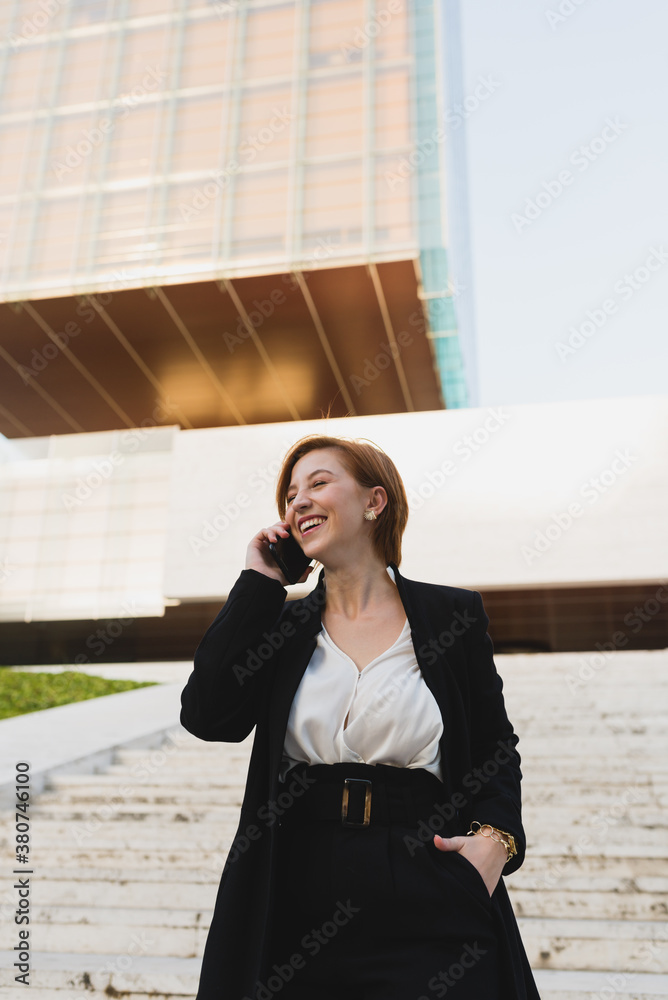 From below content female manager in elegant suit walking down the stairs in city and discussing work issues on cellphone while looking away From below content female manager in elegant suit walking down the stairs in city and discussing work issues on cellphone while looking away