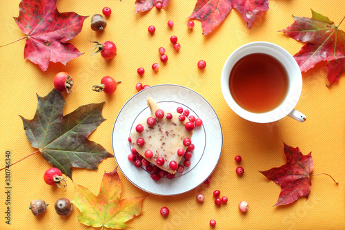 Delicious cake with cranberry berries on the background of a tea mug and autumn foliage, top view - the concept of a cozy pastime and a delicious tea party on autumn days