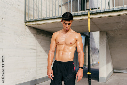 Muscular shirtless male athlete standing resting after hard workout and looking down