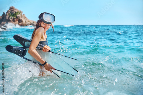 Side view of female diver in goggles and with flippers standing in waving sea photo