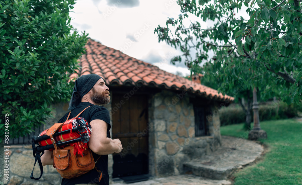 Back view of calm male tourist with backpack standing near stone house in settlement and looking away Back view of calm male tourist with backpack standing near stone house in settlement and looking away