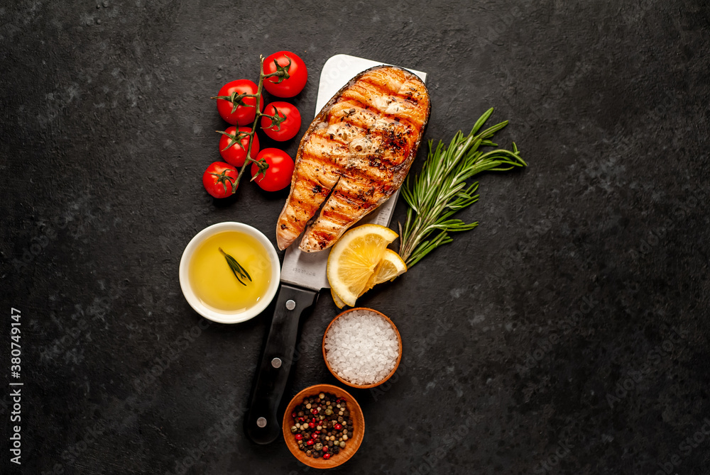 Fototapeta Grilled salmon steak with lemon and rosemary over meat knife on stone background with copy space