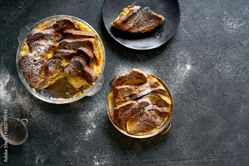 Top view of traditional bread pudding with custard, served with aromatic orange zest butter and powdered sugar on dark background photo