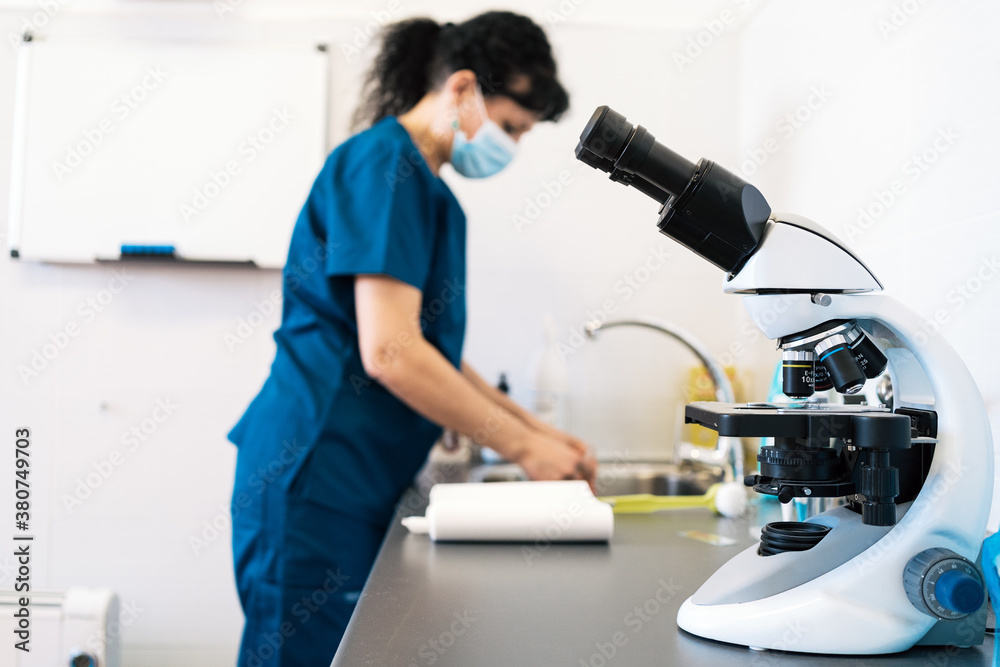 Modern microscope placed on table near female doctor in medical mask in lab of modern clinic Modern microscope placed on table near female doctor in medical mask in lab of modern clinic