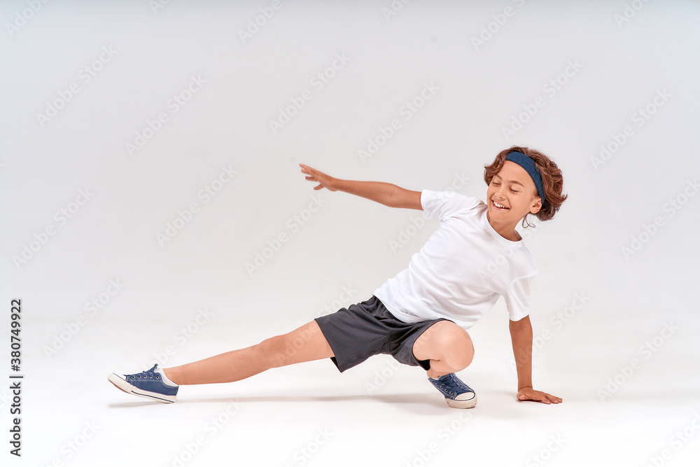 Having fun at training. Full length of a happy caucasian teenage boy in sportswear stretching legs and laughing while exercising isolated over grey background in studio