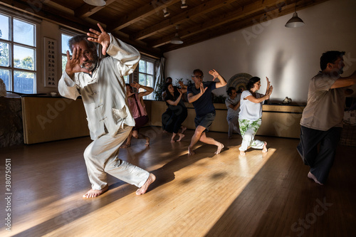 Full body of mature male instructor with group of diverse people performing chi kung pose during practice in studio
