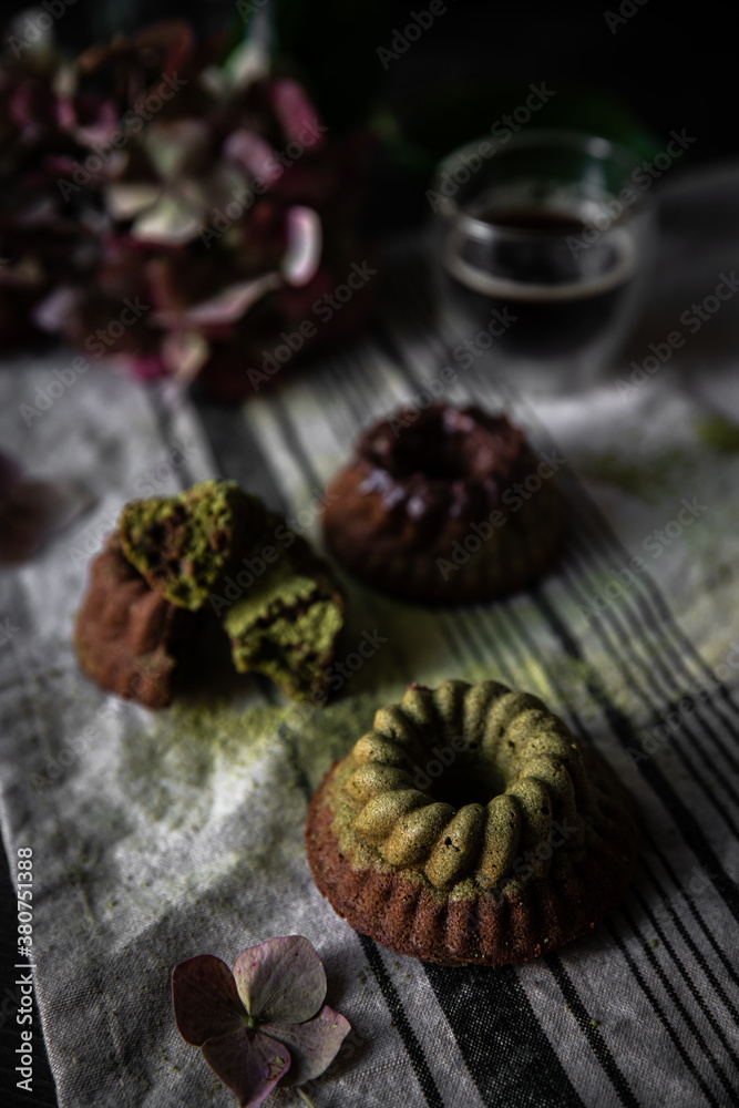 Fototapeta premium Mini chocolate-matcha bundt cakes and hydrangea flowers on linen towel on dark background.