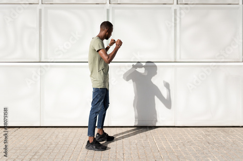 Side view of African American male standing in city in fighting position and battling with shadow on sunny day photo