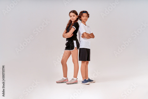 Two teenagers, cute boy and girl in sportswear looking at camera while posing isolated over grey background. Children engaged in sport