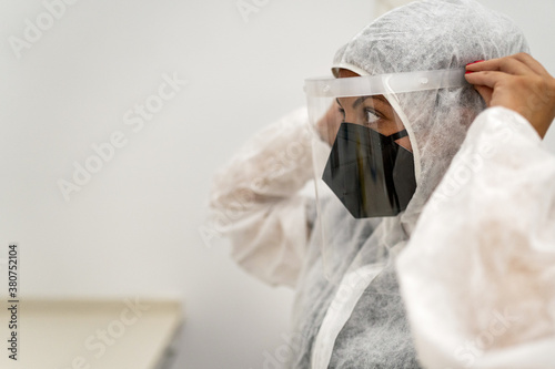 Doctor putting on protective suit with face mask while preparing for work during pandemic photo
