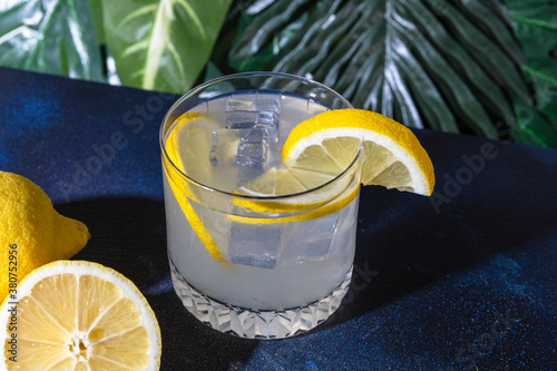 High angle of glass of cold refreshing alcohol drink with ice cubes garnished with lemon slice and placed on table in bar