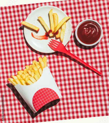 From above french fries packet near plate with potatoes soaked in ketchup