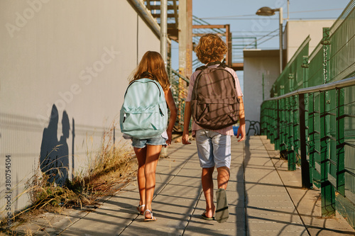 Two children with black school bags on their backs walking down an industrial passage going to school in the morning