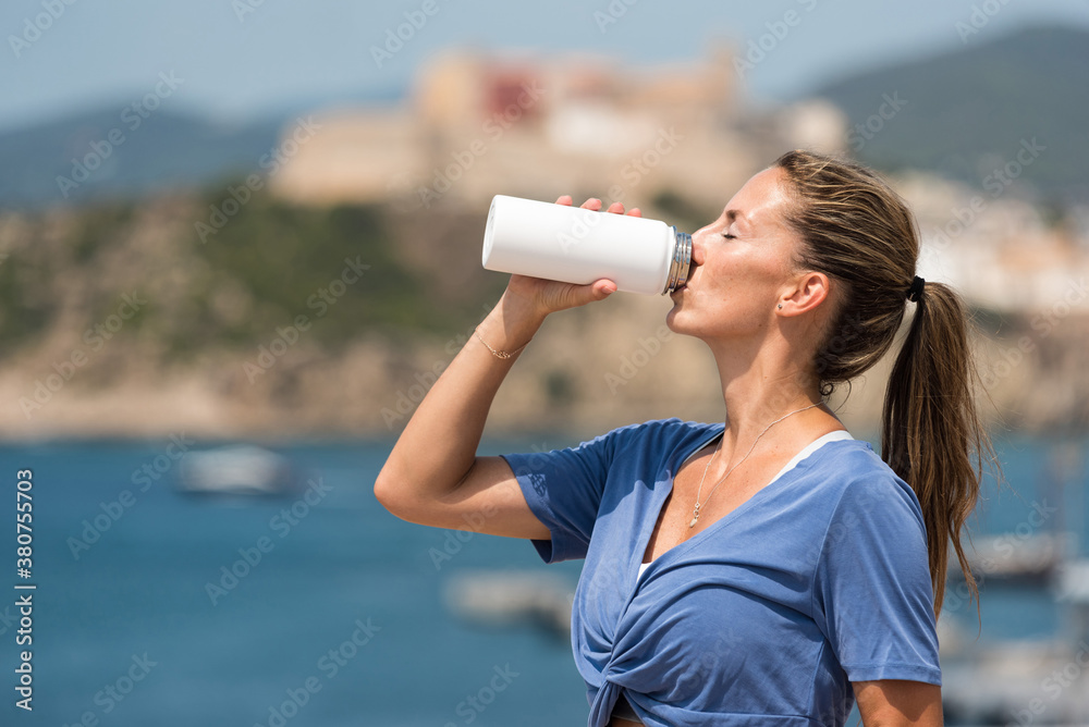 Side view of thirsty female athlete standing near sea and enjoying fresh water after workout in summer Side view of thirsty female athlete standing near sea and enjoying fresh water after workout in summer