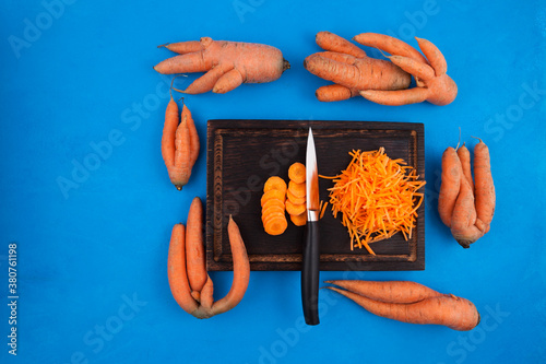 Lots of ugly carrots and grated carrots on chopping board. Blue background. Crooked vegetables of abnormal shape can be eaten. Concept - Food waste reduction. Using in cooking imperfect products photo