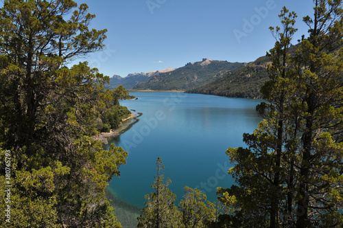 Amazing view of a lake with calm waters, surrounded by forest-covered mountains in Patagonia. Behind are snow-capped mountains