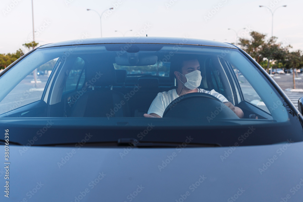 Obraz premium Chico con mascarilla dentro de coche en asiento de conductor