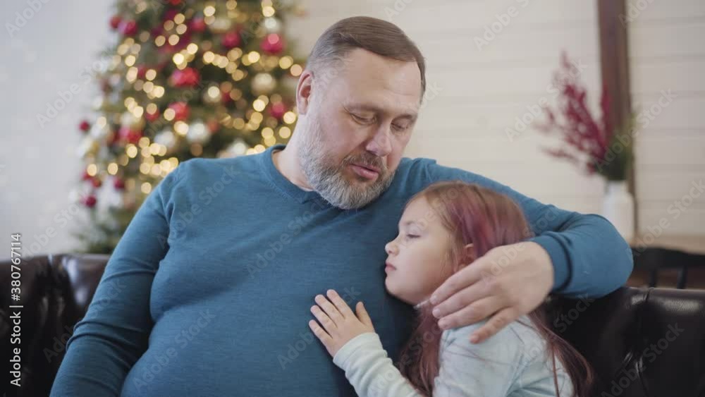 Portrait of happy mid-adult father hugging little cute daughter and talking. Cheerful Caucasian man and girl spending Christmas holidays season at home. New Year celebration concept. Portrait of happy mid-adult father hugging little cute daughter and talking. Cheerful Caucasian man and girl spending Christmas holidays season at home. New Year celebration concept.