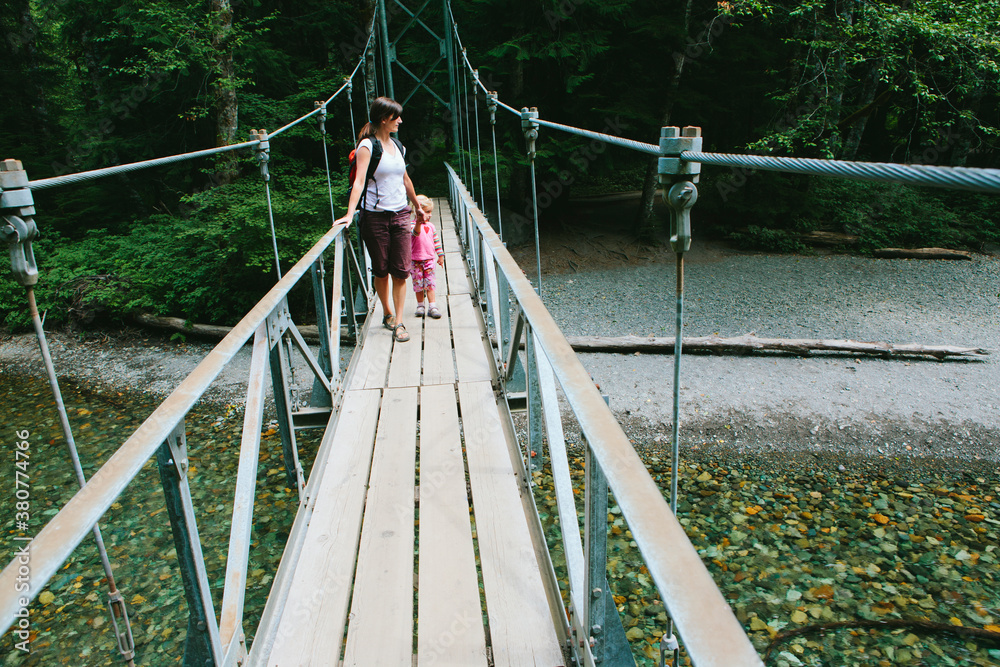 Mother and young daughter walking across suspension bridge and river Mother and young daughter walking across suspension bridge and river