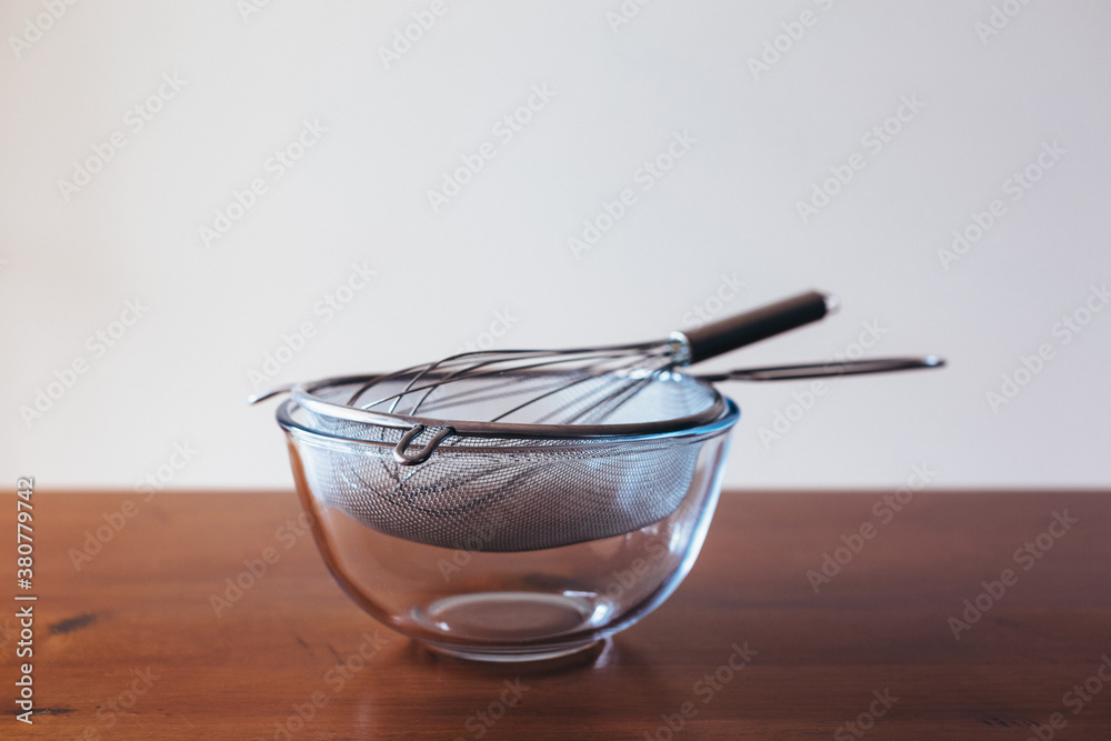 Glass bowl, sieve and whisk on a wooden table Glass bowl, sieve and whisk on a wooden table