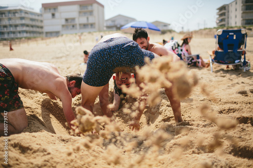 A group of rowdy friends dig violently in the sand on the beach photo