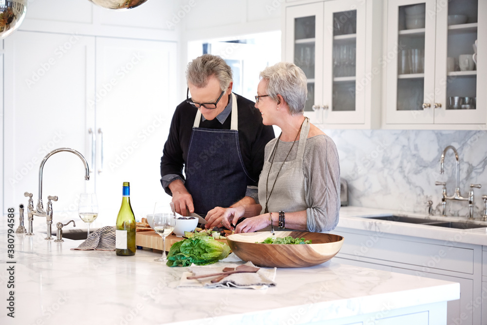 Mature couple with grey hair cooking in kitchen of luxury home