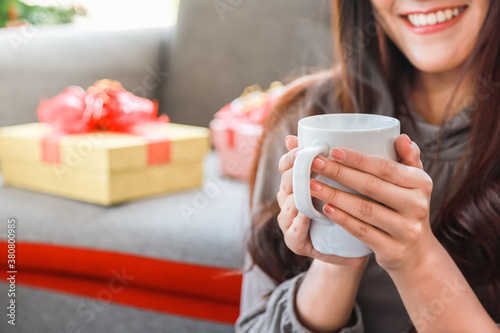 Closeup of young woman holding white mug cup of coffee with beautiful giftbox as background