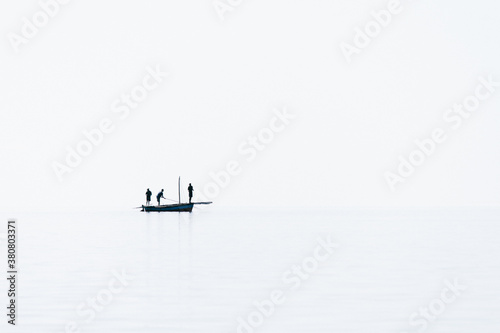 Silhouette of a small boat and three fishermen on calm water on the sea photo