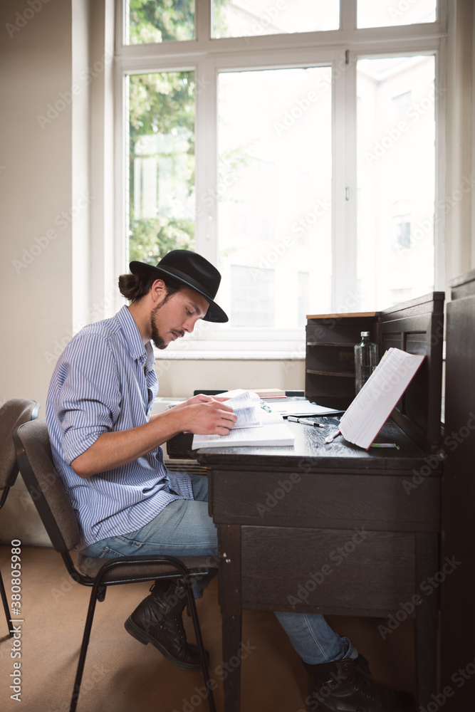Male college student learning at a desk under the window Male college student learning at a desk under the window