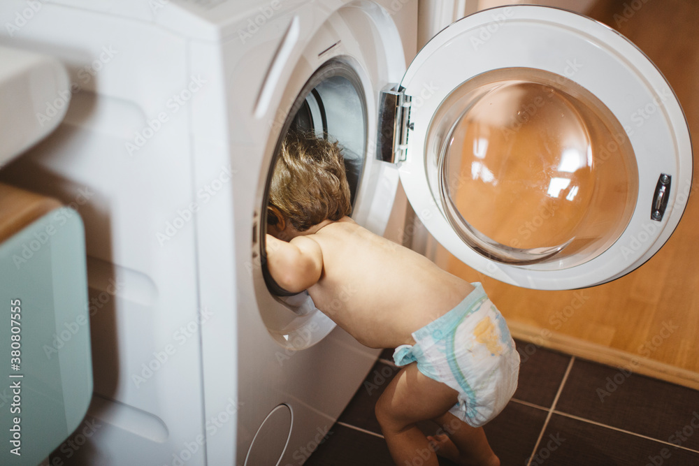 Young child in nappy climbing inside a washing machine Young child in nappy climbing inside a washing machine